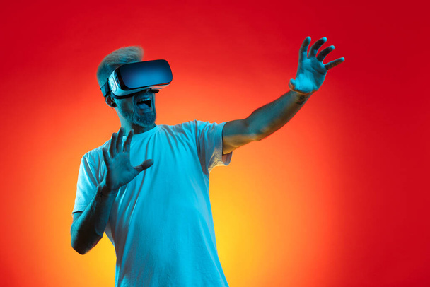 Screaming bearded hipster man with blonde hair wearing virtual reality goggles in studio in neon lights. - Foto, Imagen