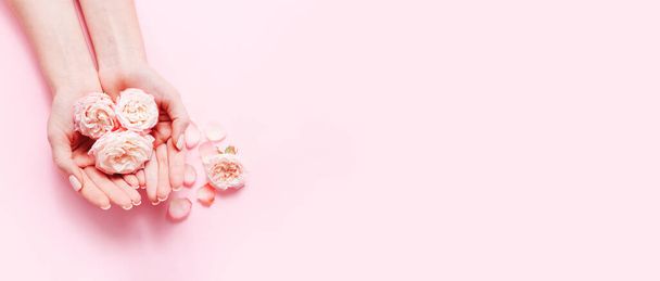 Mani delle donne con manicure alla moda con rose rosa su sfondo rosa, vista dall'alto. - Foto, immagini