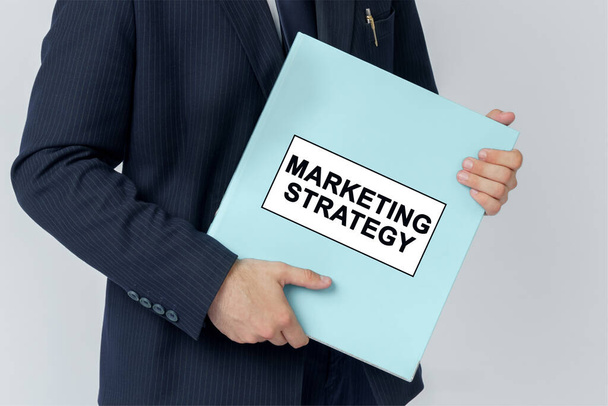 Business concept. A businessman holds a folder with documents, the text on the folder is - MARKETING STRATEGY - Foto, imagen
