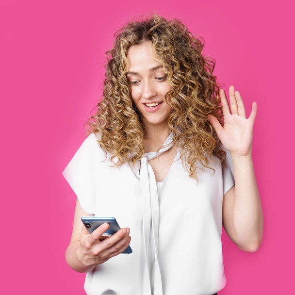 Young woman communicates through the phone by video link, expressing emotions. Female portrait. Isolated on pink background - Foto, imagen
