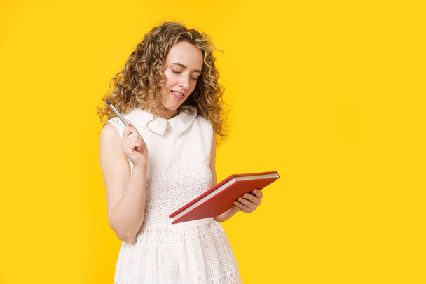 A young woman holds a textbook and a pen. Female portrait. Isolated on yellow background - Fotó, kép