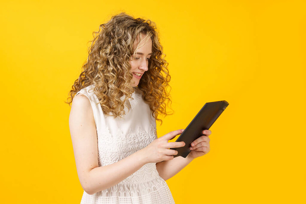 Portrait of a young woman who communicates on a tablet. Female portrait. Isolated on yellow background - Foto, afbeelding