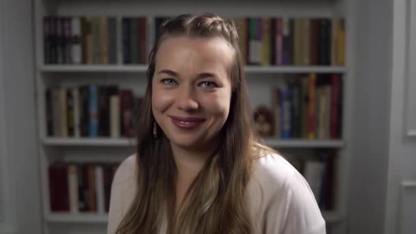 Psychologin lächelt und nickt und kokettiert mit Porträt vor Bücherhintergrund - Filmmaterial, Video