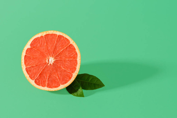 Half of ripe juicy pink grapefruit and two leaves with shadow on a green background. Organic antioxidant. Vegetarian, raw food diet and healthy eating. Copy space. - Fotografie, Obrázek