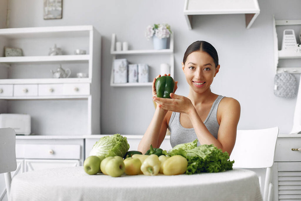 Beautiful and sporty girl in a kitchen with a vegetables - Foto, Imagen