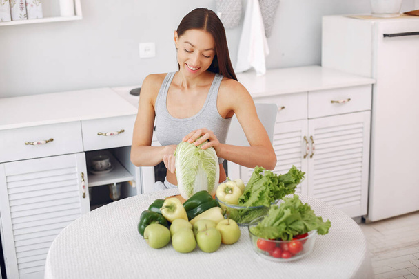 Beautiful and sporty girl in a kitchen with a vegetables - Photo, image