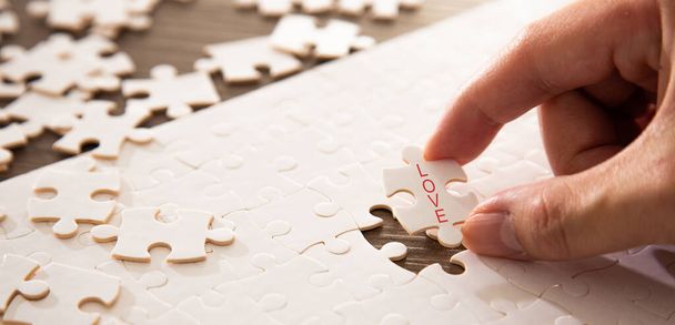 Hand completing the a last piece of jigsaw puzzle with love word. Family love conceptual - Photo, Image