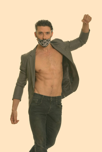 Studio shot of young handsome bearded businessman wearing mask and shirtless against white background - Photo, Image