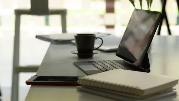 オフィスルームの白いテーブルの上にデジタルタブレット、ノートブック、スマートフォンや電源とワークスペースの側面図  - 写真・画像