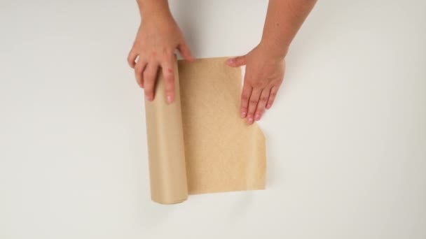 mujer sosteniendo un rollo de papel pergamino marrón y arrancando una pieza, fondo blanco, vista superior - Metraje, vídeo