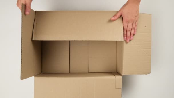 mano femenina abre caja de cartón marrón y se llena con relleno blanco para un transporte seguro, vista superior, concepto móvil - Imágenes, Vídeo