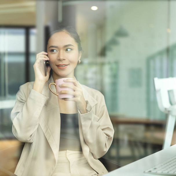 Widok przez okno kobiety przedsiębiorcy rozmawia przez telefon podczas przerwy w biurze - Zdjęcie, obraz