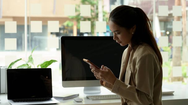 Portret van een vrouwelijke ondernemer die sms 't op een smartphone terwijl hij aan het bureau zit met digitale apparaten in de kantoorruimte  - Foto, afbeelding