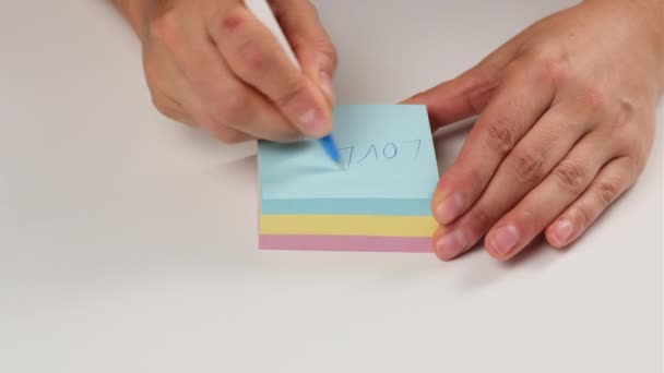 θηλυκό χέρι γράφει με λέξεις στυλό σε πολύχρωμα αυτοκόλλητα χαρτί, κοντά - Πλάνα, βίντεο