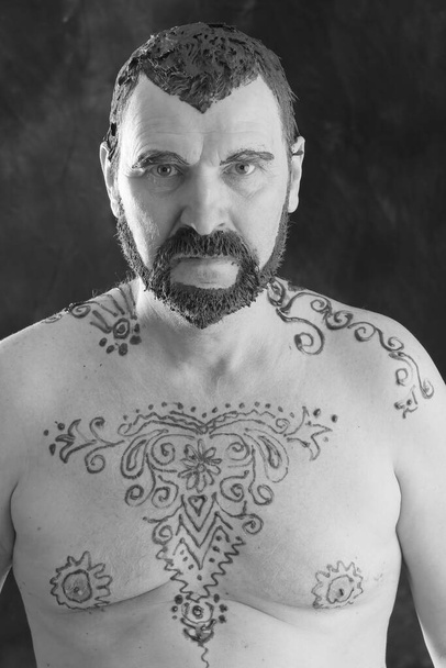 close-up portrait of an adult male with a naked torso and body painting with henna and colored hair and beard studio - Foto, Imagen