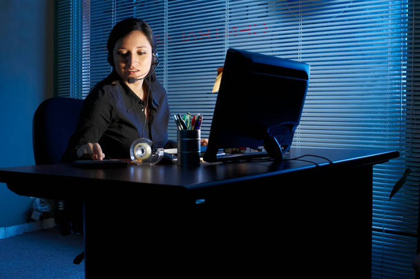 Νεαρή Λατίνα που κάθεται στο δωμάτιό της ή στο γραφείο της και εργάζεται σε υπολογιστή αργά ή νωρίς το πρωί - Φωτογραφία, εικόνα