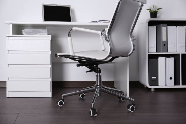Comfortable rolling chair near table with laptop in modern office - Фото, изображение