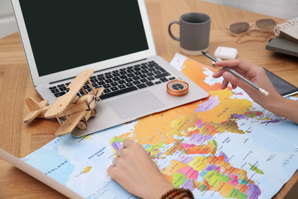 Woman with world map and laptop planning trip at wooden table, closeup - Фото, изображение