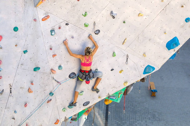 Uma mulher sobe uma parede de escalada, um alpinista está treinando em terreno artificial, escalada na cidade, uma garota forte, esportes na cidade, segurança em esportes radicais. - Foto, Imagem