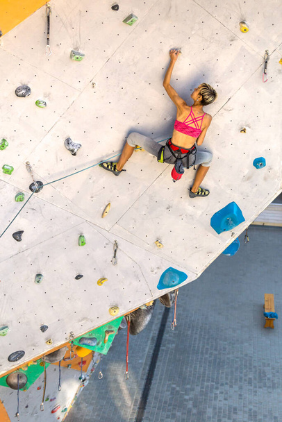 Egy nő mászik a mászófalra, egy hegymászó mesterséges terepen edz, sziklát mászik a városban, egy erős lány, sport a városban, biztonság extrém sportokban. - Fotó, kép