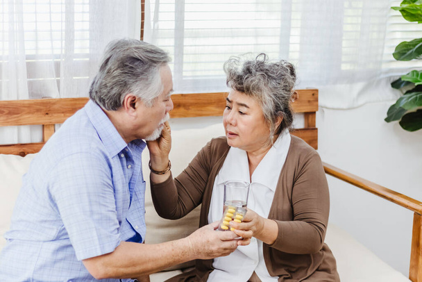 Asian couple woman caring sick elderly man by giving pill or drug at home. Love and relationship of retired senior couple. Health care and medicine of illness aged people photo concept. - Foto, Imagem