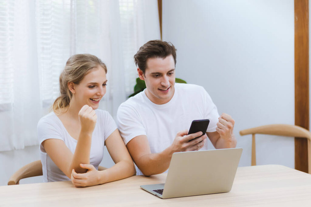 Усміхнена кавказька пара святкує разом успіх підприємницького бізнесу в Інтернеті або досягнення роботи або освітній екзамен результату через смартфон вдома. Концепція фотографії в Інтернеті та технології
 - Фото, зображення