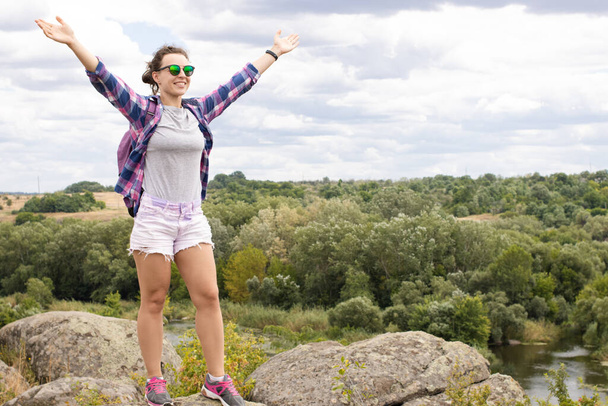 Lachende vrouwelijke wandelaar met rugzak open armen uit bij bergtop, staan op de rots en genieten van het landschap uitzicht op het landschap. Sterk en vrij, reizen avontuur concept.  - Foto, afbeelding