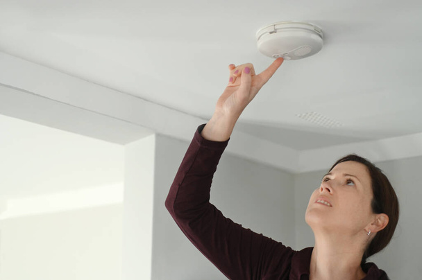 Young adult woman (age 25-35) checking fire alarm at home. - Fotoğraf, Görsel