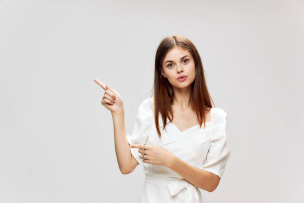 Woman with long hair gestures with her hands pointing to the top of a white dress Copy Space - Photo, Image