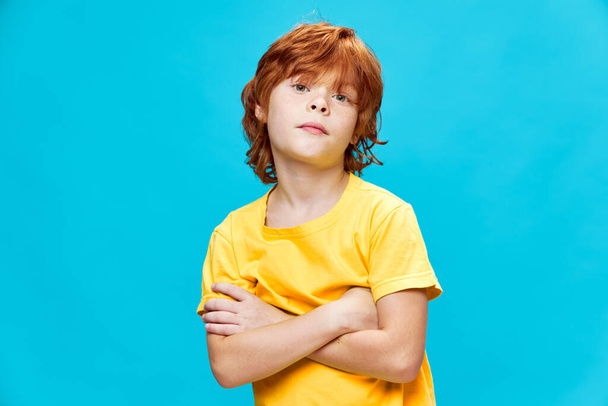 Red-haired boy crossed his arms on his chest and wrinkled yellow T-shirt background - Photo, Image