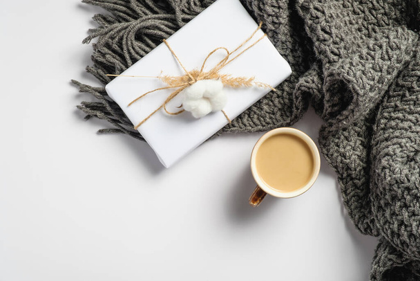 Cup of coffee, gift box and knitted scarf on white background. Hygge style flat lay composition, autumn fall concept. Top view cozy home desk. - Fotografie, Obrázek