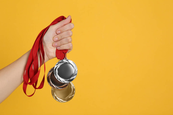Woman holding medals on yellow background, closeup. Space for design - Photo, Image