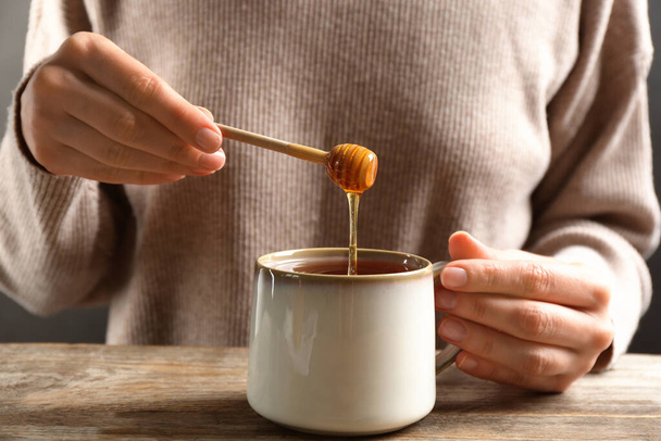 Woman putting honey into tea at wooden table, closeup - Фото, изображение