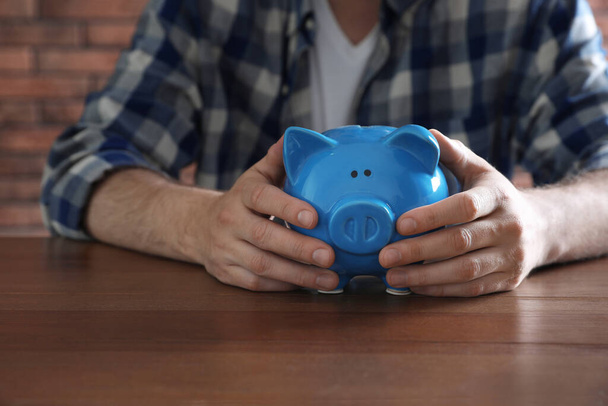 Man with piggy bank at wooden table, closeup - 写真・画像