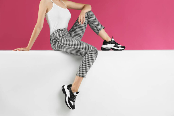 Woman in stylish sneakers sitting on color background, closeup - Photo, Image