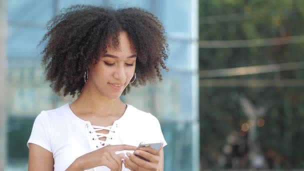 Smiling young afro american woman with interest looks into smartphone, excitedly happily points finger at screen of gadget phone, getting ecstasy of unexpected joy, wow emotions in urban modern city. - Footage, Video