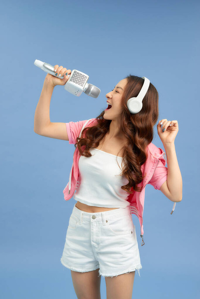 Прекрасна азіатська дівчина з мікрофоном і навушниками ізольована на синьому фоні.. - Фото, зображення