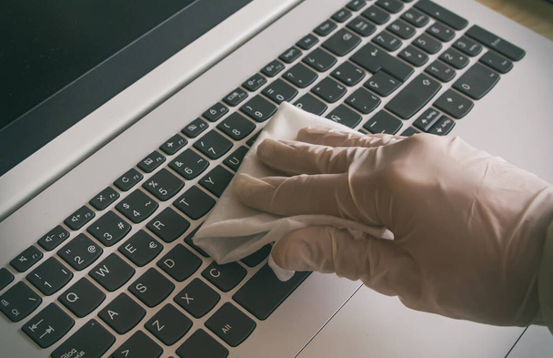 Vrouw die de laptop thuis schoonmaakt met handschoenen aan en een ontsmettingsdoekje gebruikt om ervoor te zorgen dat het oppervlak vrij is van het Covid-19 virus - Foto, afbeelding