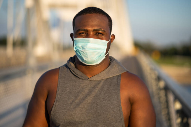 Porträt eines jungen afrikanisch-amerikanischen Mannes mit Schutzmaske im Gesicht. Verantwortungsbewusstes Verhalten bei der Pandemie des Coronavirus. - Foto, Bild