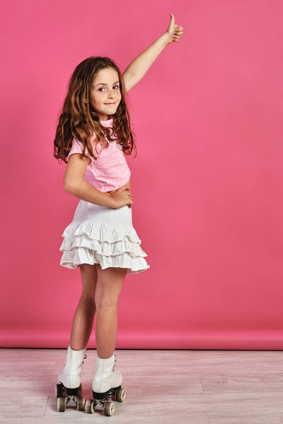 A vertical shot of a little girl in roller-skates posing and gesturing the like sign - Photo, image