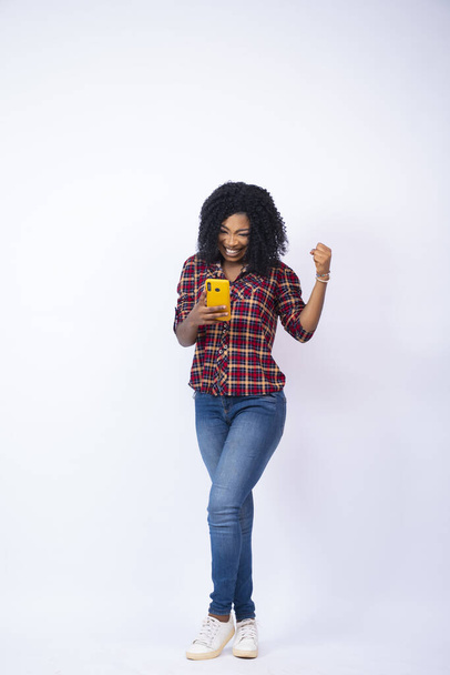A vertical shot of a black female feeling happy looking at her phone - Fotografie, Obrázek