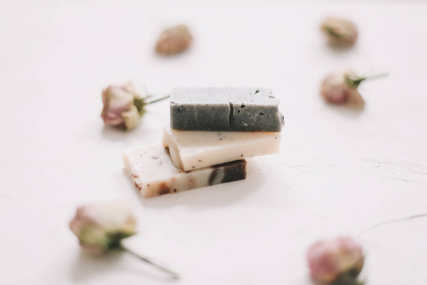 Soap bars with dry roses on white background. Handmade floral soap with rose buds. Natural cosmetics. flat lay, top view - 写真・画像
