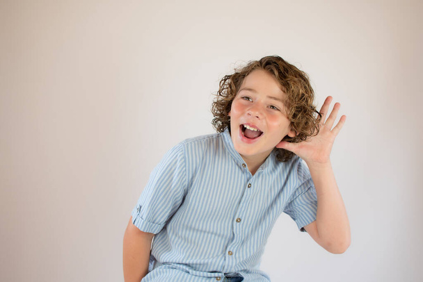 Αγόρι με μπλε πουκάμισο κάνει την χειρονομία ακρόασης χαμογελώντας - Φωτογραφία, εικόνα