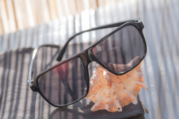 Retro aviator sunglasses model with black lenses on a shell in a summer day closeup . Selective focus - 写真・画像