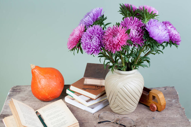aster flores ramo, libros y manzana sobre fondo artístico, bodegón, concepto del día del maestro - Foto, Imagen