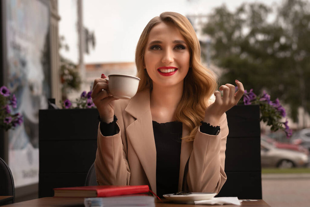 Carefree modern girl with long blonde hair with cup drinking coffee at city street cafe terrace and dreaming, lifestyle concept - Photo, Image