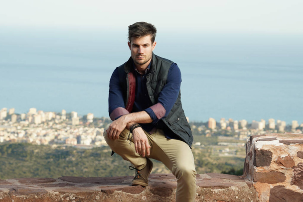 A beautiful shot of a stunning male leaning on his leg with a blurred city view behind - Foto, Bild