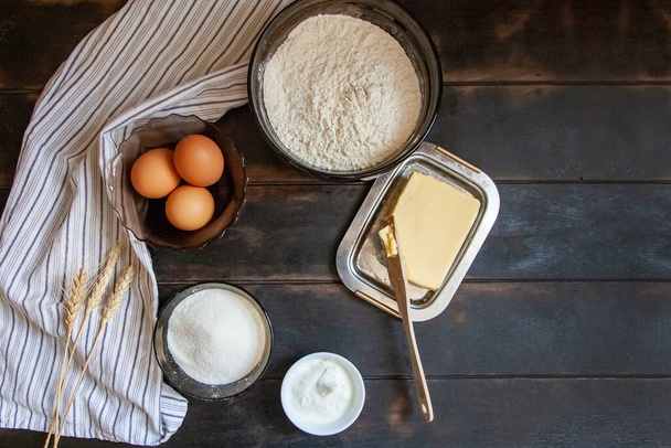 Baking ingredients for shortcrust pastry: butter, flour, eggs, sour cream, a towel on a wooden background. Flatley top view. - Photo, Image