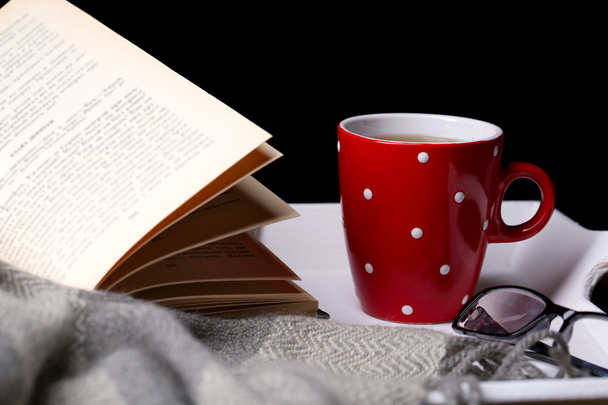 Cup of hot tea with book and plaid on table on dark background - Photo, image