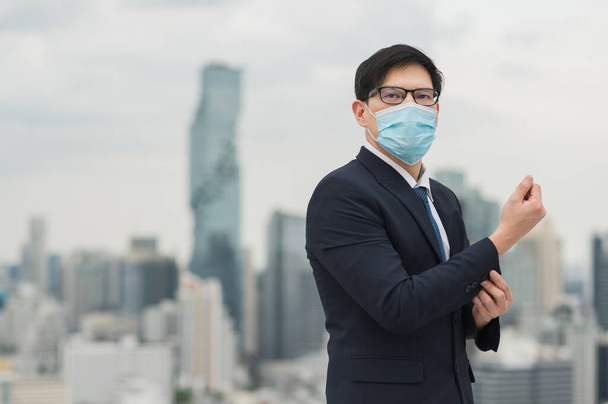 Jonge knappe Aziatische zakenman met een masker om de vervuiling en het virus te beschermen bij het bouwen van stedelijke steden achtergrond. - Foto, afbeelding